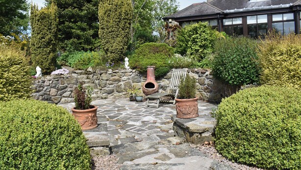 A stone patio with potted plants, a stone wall, and a wooden bench.