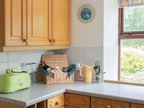 A kitchen with wooden cabinets, a green toaster, a wicker basket with bottles, a milk clock, and a window with greenery outside. - Middle Lodge enjoys a rural, south facing setting and is a gardener’s delight. (Near Mintlaw)