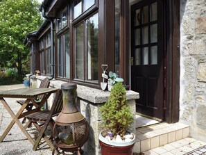 A stone building with a wooden deck, a metal lantern, and a small potted plant. - Middle Lodge enjoys a rural, south facing setting and is a gardener’s delight. (Near Mintlaw)
