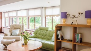 A living room with a green sofa, a beige armchair, a wooden coffee table, and a bookshelf with books and decorative items.