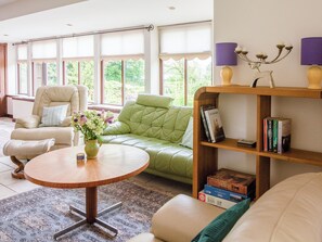 Un salon avec un canapé vert, un fauteuil beige, une table basse en bois et une bibliothèque contenant des livres et des objets décoratifs.