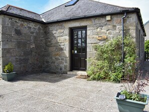 A stone building with a black door, a sign reading 'Middle Lodge,' and a small garden area with potted plants.