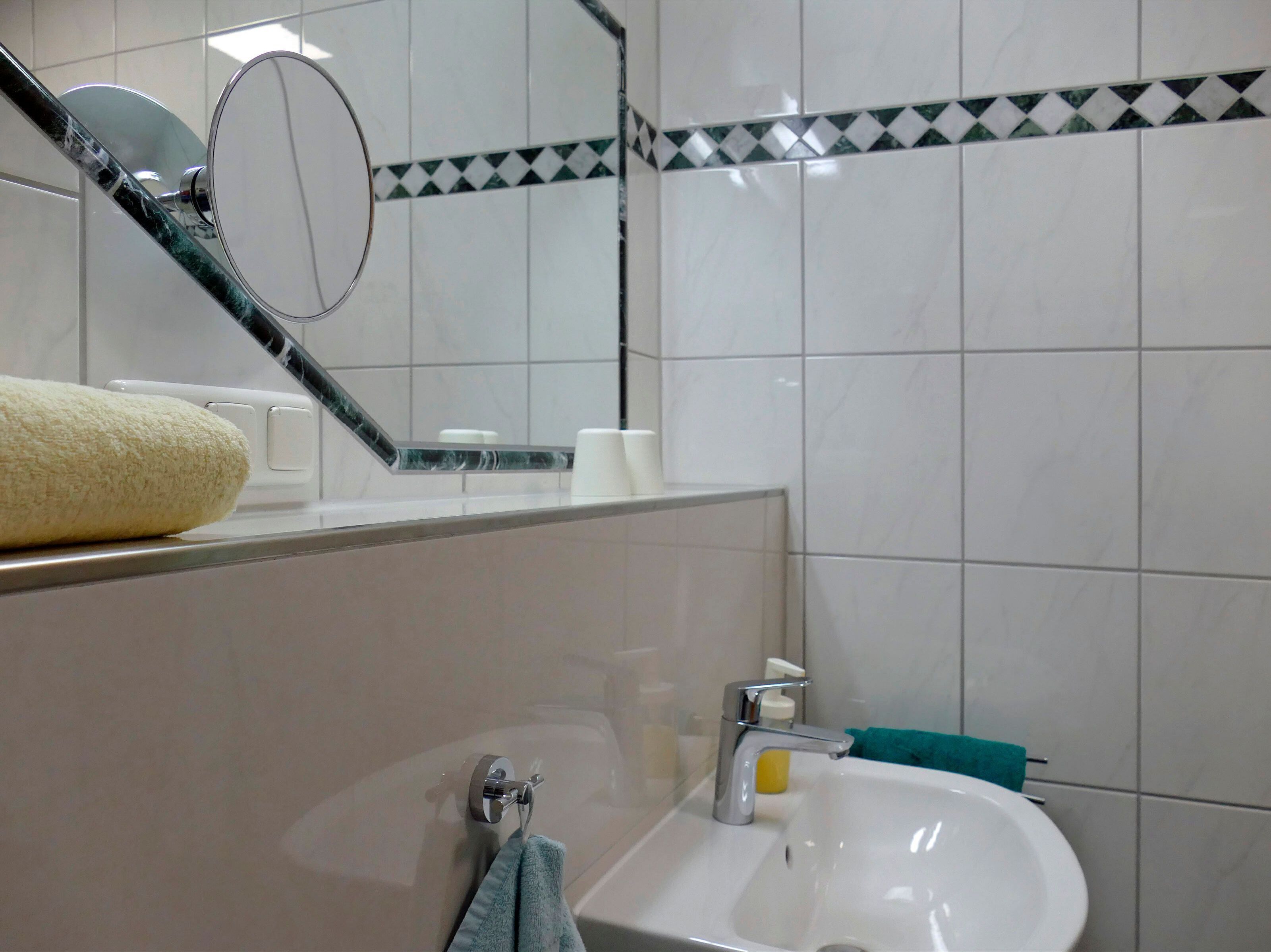 Un baño con lavabo, espejo y perchero para toallas.
