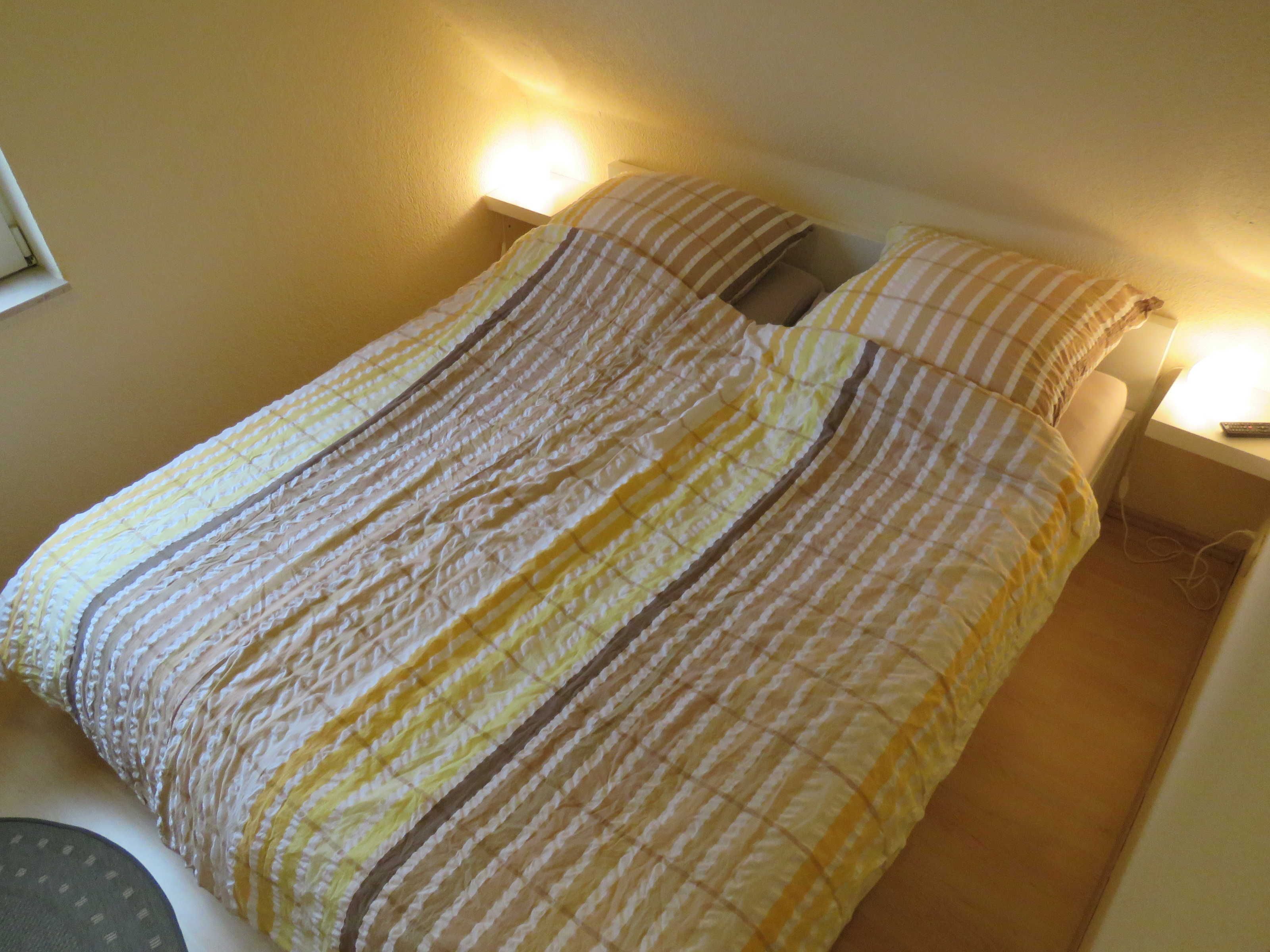 Un lit avec une couvre-lit à rayures, deux oreillers et des lampes de chevet.