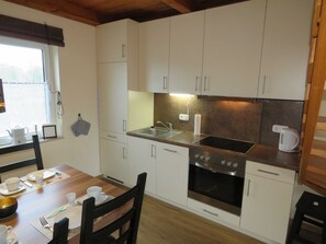 A compact kitchen with white cabinets, a stainless steel sink, a built-in oven, and a dining table set for two.