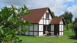 A traditional half-timbered house with a sloped roof, a small patio with a table and chairs, and a well-maintained lawn.