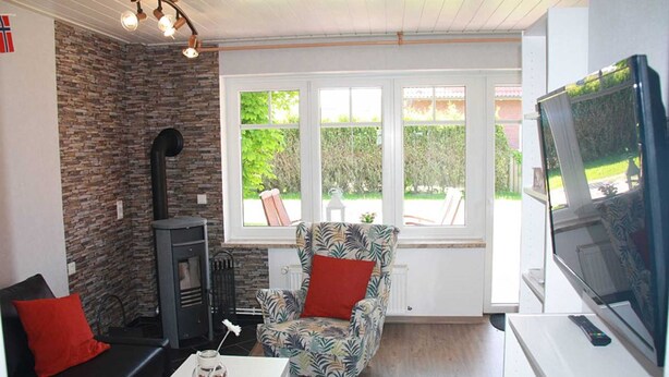 A cozy living room with a stone wall, a fireplace, a patterned armchair, a sofa, and a television. - Vacation rental Norway - House Nordic Dreams (Esens)