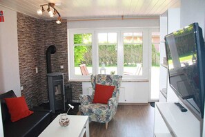 A cozy living room with a stone wall, a fireplace, a patterned armchair, a sofa, and a television. - Vacation rental Norway - House Nordic Dreams (Esens)