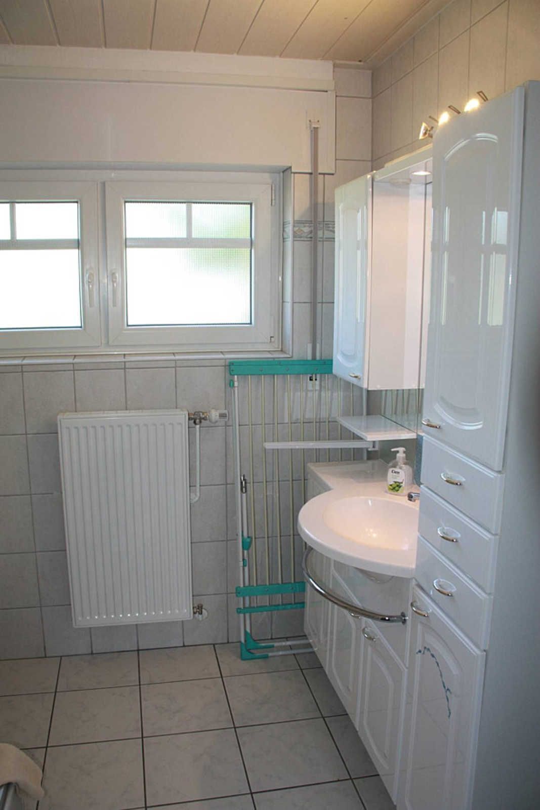 A bathroom with a white radiator, a sink, a mirror, and cabinets.