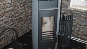 A wood-burning stove with a chimney, set against a stone wall. - Vacation rental Norway - House Nordic Dreams (Esens)