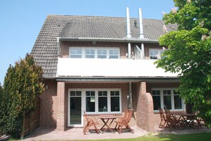 A two-story brick house with a tiled roof, a patio with wooden furniture, and a chimney.