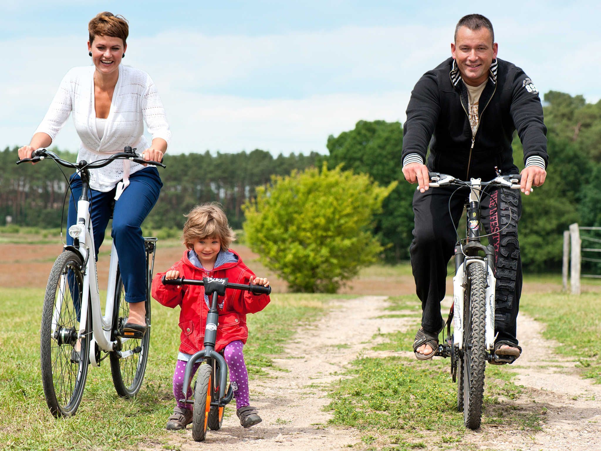 Eine Familie fährt mit Fahrrädern auf einem Feldweg, im Hintergrund grüne Landschaft.