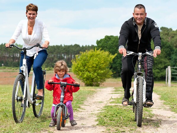 A family on bicycles on a dirt path with greenery in the background.