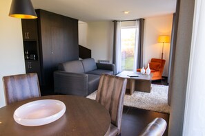 Un salon moderne comprenant un canapé, une table à manger avec des chaises, une table basse, une lampe et une vue sur l’extérieur.