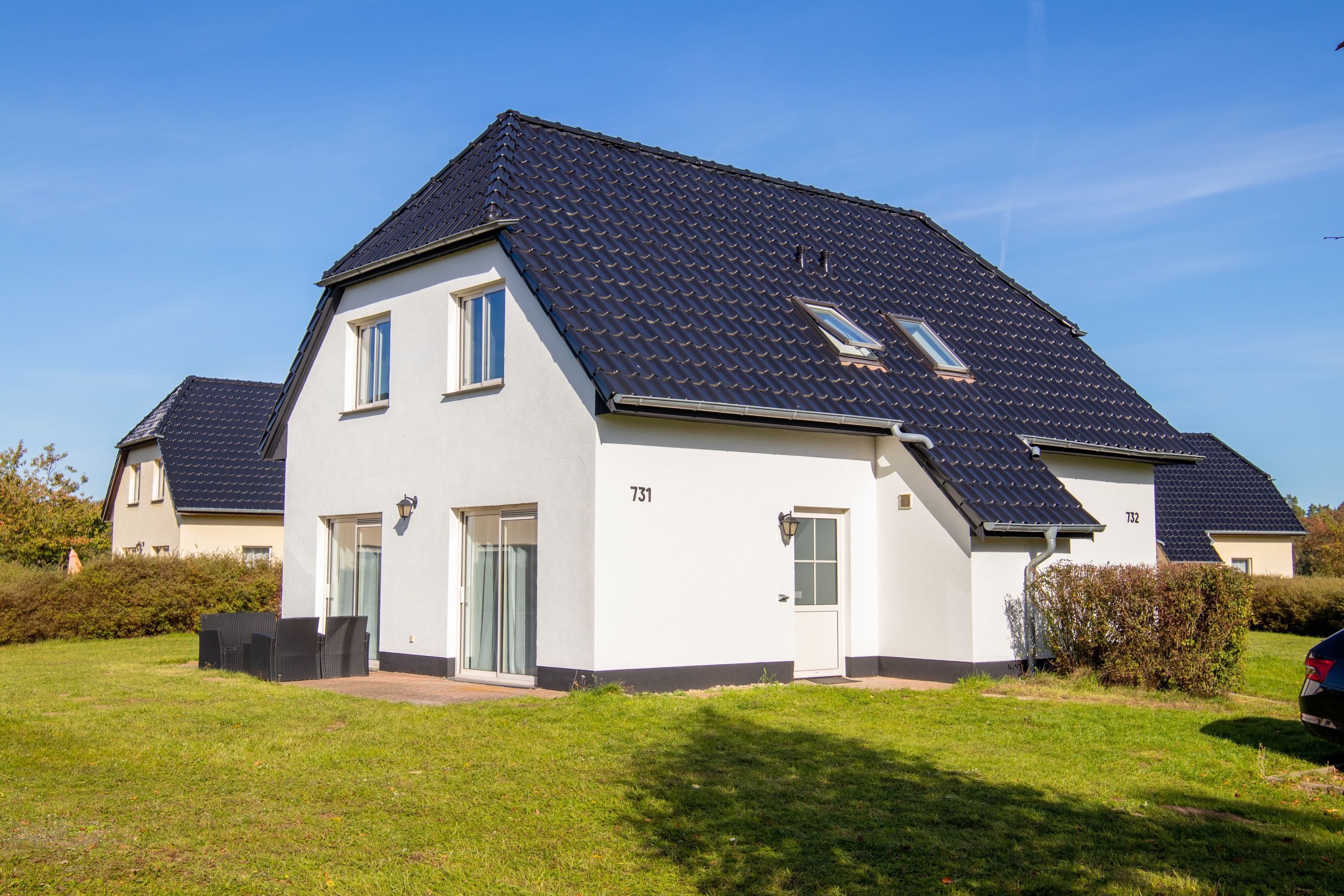 Een woonhuis met twee verdiepingen, een donker betegeld dak, een voordeur en een klein raam.