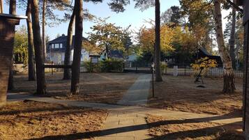A residential area with a paved walkway, tall trees, and houses in the background.