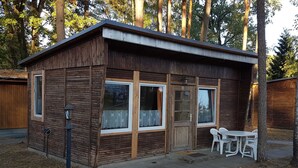 Una pequeña cabaña de madera con un porche, una mesa con sillas y una ventana con cortina.