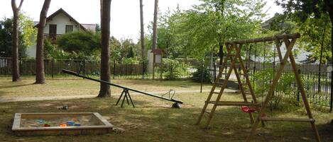 A backyard with a seesaw, a swing set, and a sandbox.