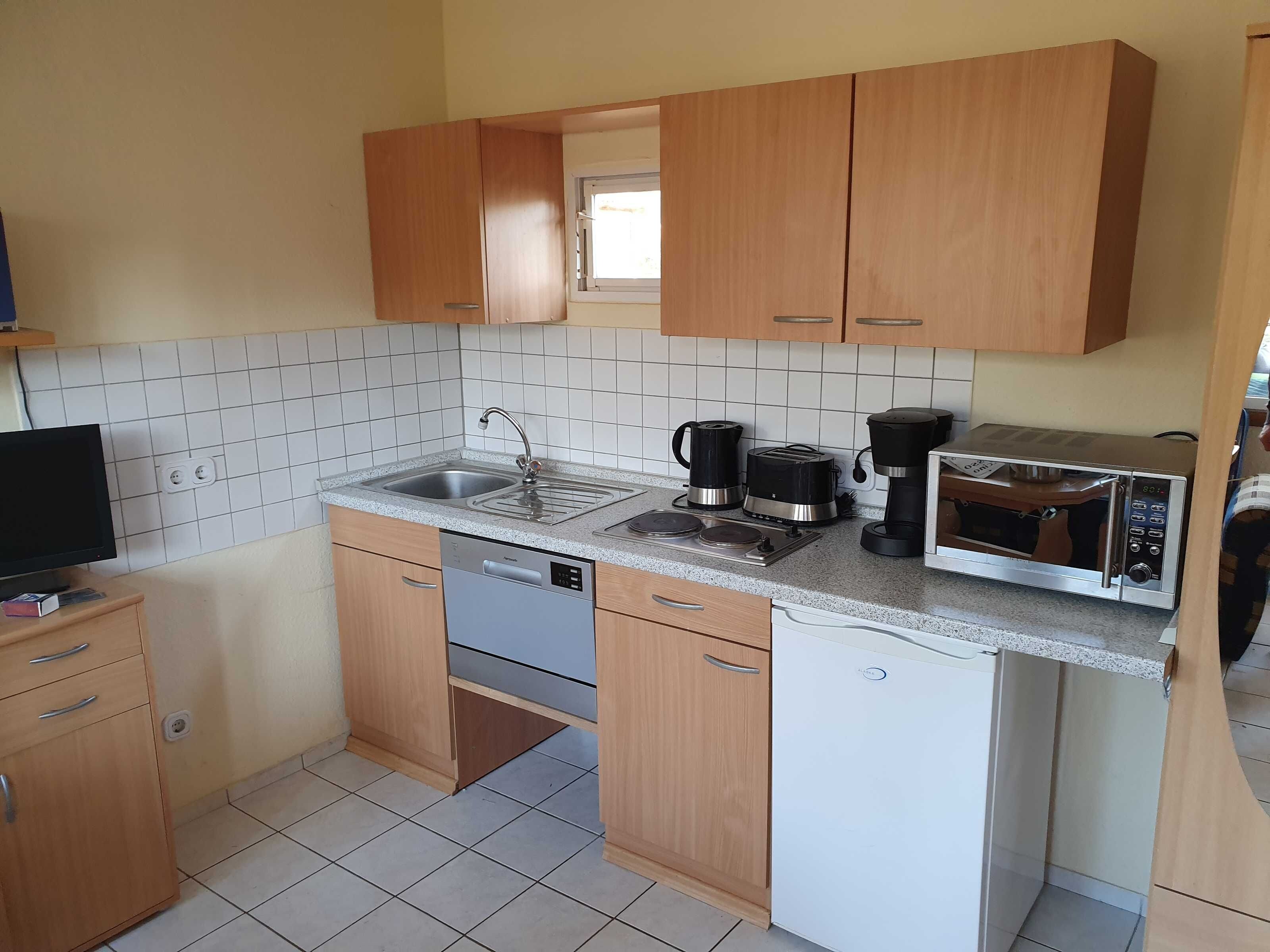 Eine kompakte Küche mit Holzschränken, einem Geschirrspüler, einer Mikrowelle, einem Toaster und einer Kaffeemaschine.