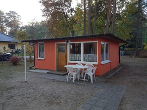 Un piccolo edificio a un piano con facciata rossa e dettagli bianchi, dotato di una porta in legno e ampie finestre. Presenta inoltre una piccola zona patio con tavolo e sedie.