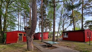 Un campamento con cabañas rojas, una mesa de picnic y sillas de plástico blancas.