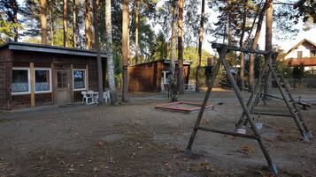 A rustic cabin with a wooden exterior, a small patio with outdoor seating, and a swing set in a wooded area.
