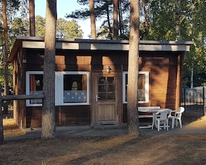 Une petite cabane en bois, dotée d’une seule porte et de deux fenêtres, entourée d’arbres.