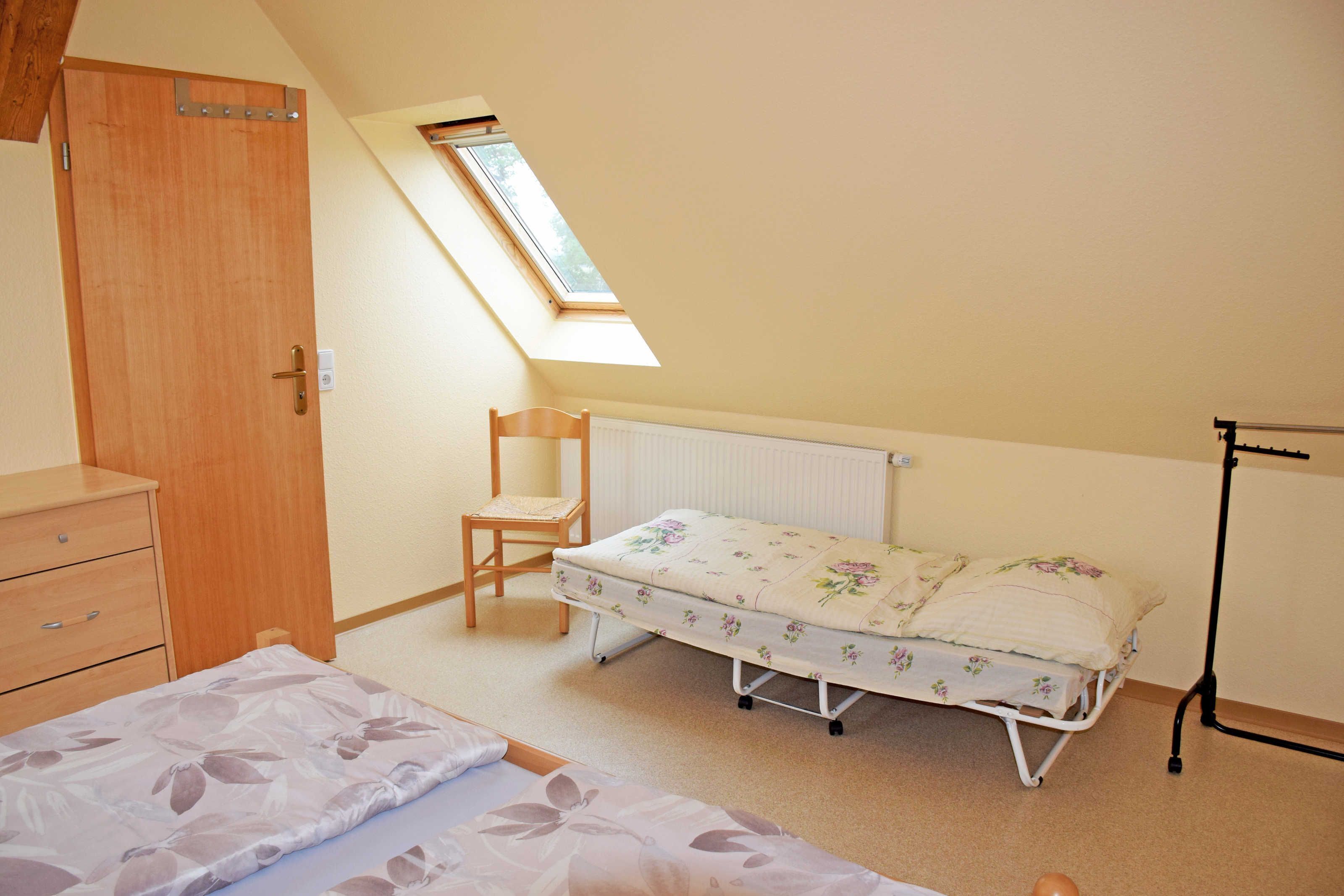 A bedroom with a wooden wardrobe, a single bed with a floral mattress, a chair, a radiator, and a skylight.