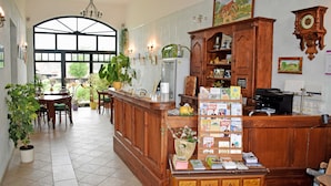 A reception area with a wooden counter, potted plants, a large window, and a wall clock. - 06 Apartment - Ferienhof auf Rgen (Putbus)