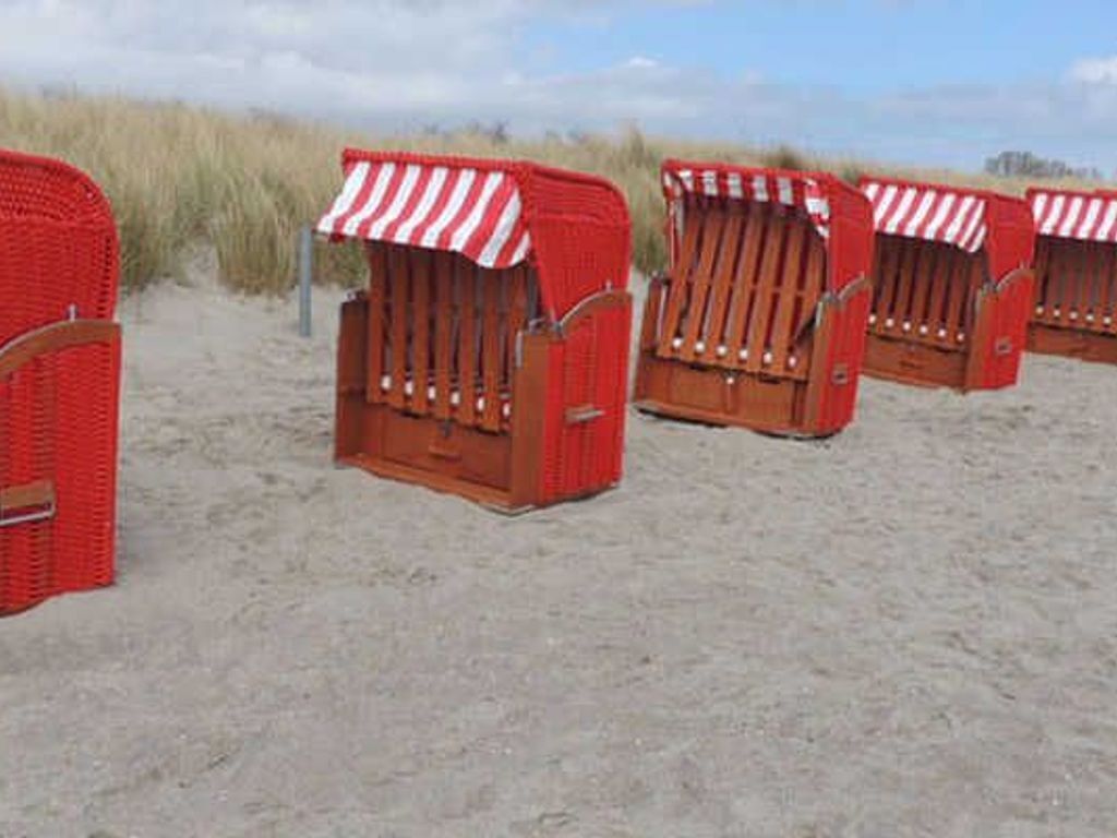 Des cabanes de plage dotées d’auvents à rayures, disposées en rangée sur un terrain sablonneux.