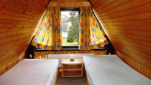 A cozy attic bedroom with two single beds, a small table, and a window with floral curtains. - Summer house, rowing boat incl. - Summer house (Krakow am See)