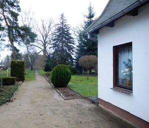 A pathway leading to a white building with a window displaying a vase of flowers. - Summer house, rowing boat incl. - Summer house (Krakow am See)