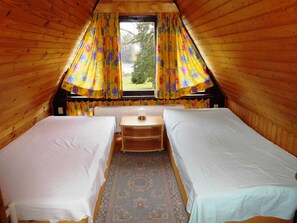 A cozy attic bedroom with two single beds, a small table, and a window with floral curtains. - Summer house, rowing boat incl. - Summer house (Krakow am See)