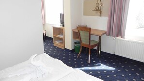 Une chambre d’hôtel avec un lit, un bureau et une chaise, une télévision et une fenêtre avec des rideaux.