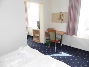 Une chambre d’hôtel avec un lit, un bureau et une chaise, une télévision et une fenêtre avec des rideaux.