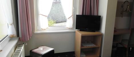 A small room with a window, a television on a wooden stand, a radiator, and a patterned carpet.