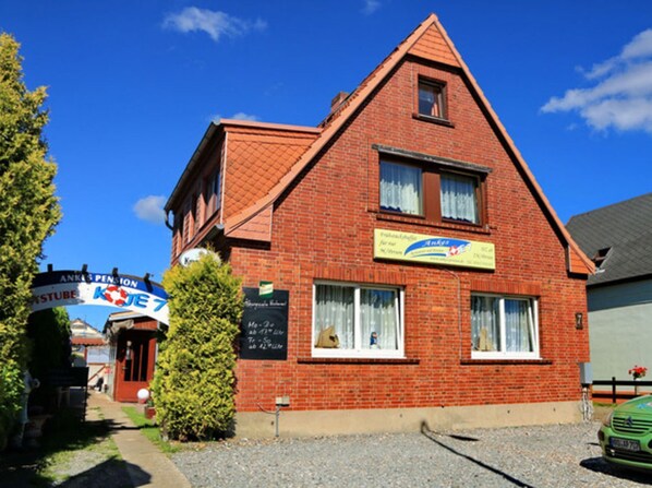A red brick building with a triangular roof, a signboard, and a green car parked in front.