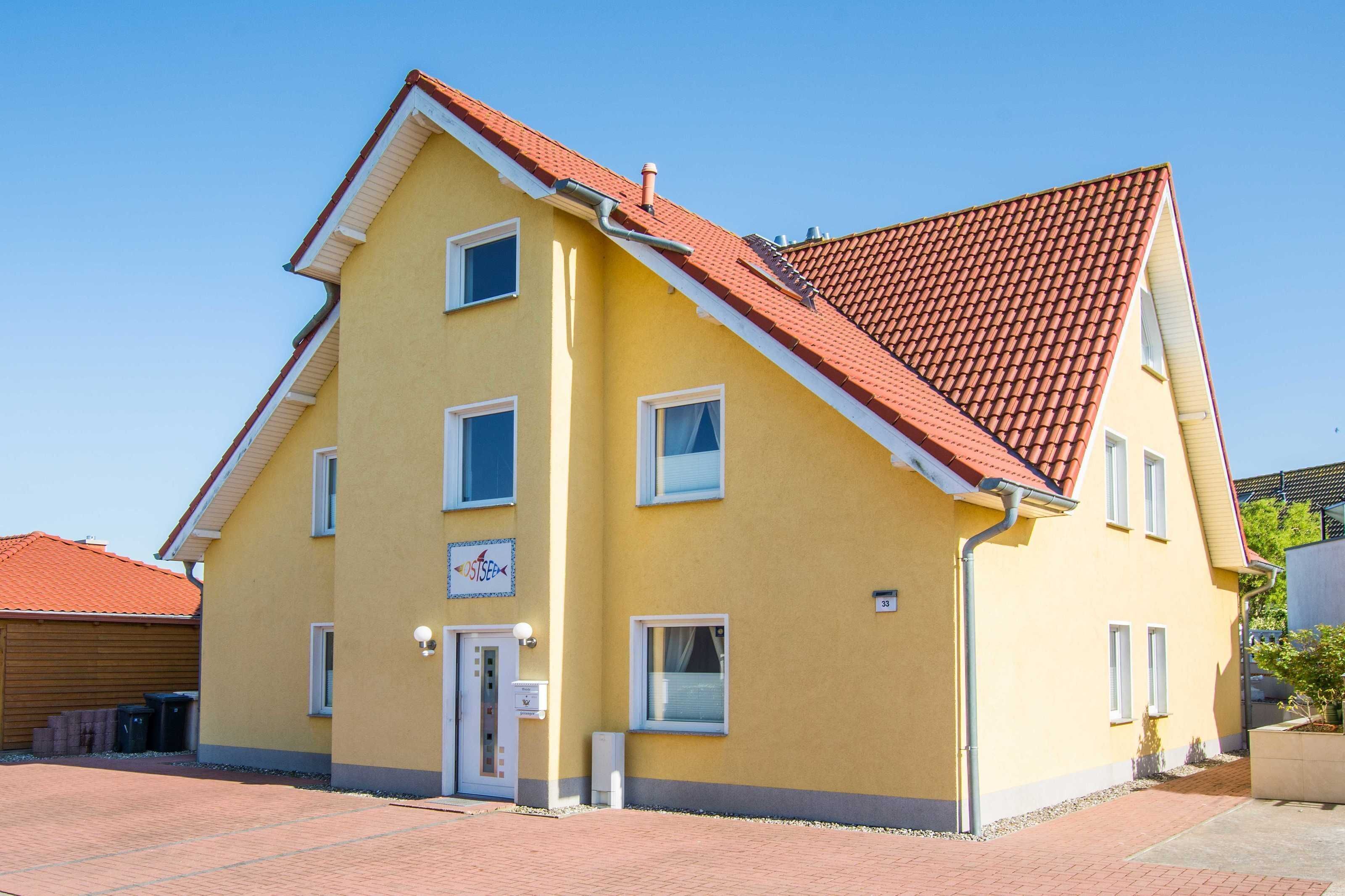 A yellow building with a red-tiled roof, a door, and windows.