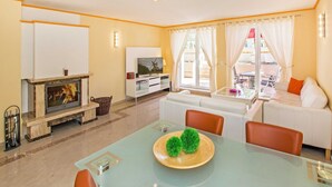 Un salon avec une cheminée, des canapés blancs, une table à manger en verre et un téléviseur posé sur un meuble blanc.