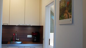 A kitchen with wooden cabinets, a sink, a coffee maker, and a framed picture on the wall. - Double room 08 - Guest house & beach hall (Ahrenshoop)