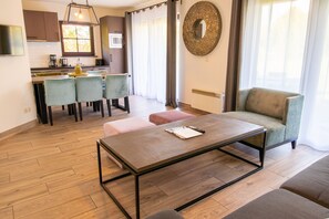 Una sala de estar moderna con una mesa de centro de madera, un sofá y un comedor con sillas, con una cocina al fondo.