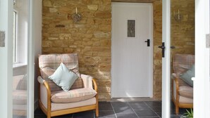 Una habitació acollidora amb una paret de pedra, una porta blanca i una cadira de fusta amb coixí escocès.