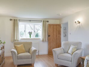Una habitación con dos sillones, una puerta de madera, una ventana con cortinas y una lámpara fijada a la pared.