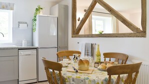 Una cuina amb taula de menjador preparada per a dues persones, un frigorífic i una finestra amb vista a vegetació.