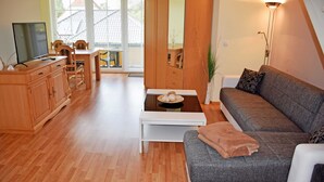 Een moderne woonkamer met een grijze bank, een houten eettafel en een televisie op een houten kast.