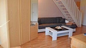 Een moderne woonkamer met een houten vloer, een grijze bank, een witte salontafel en een houten kast.