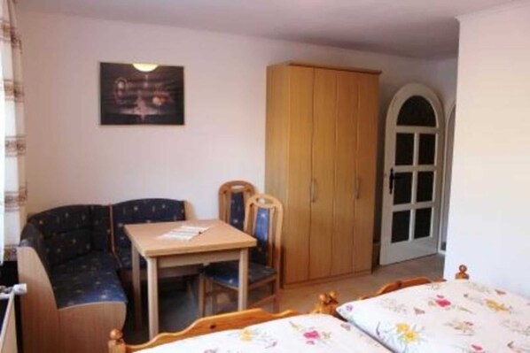 A small, cozy room with a bed, a chair, a table, and a wardrobe.