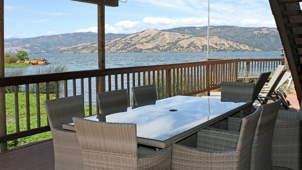 Una terrazza esterna con mobili in vimini e vista su un lago e delle colline.