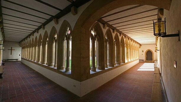 Un largo pasillo con ventanas de arco y suelo de baldosas.