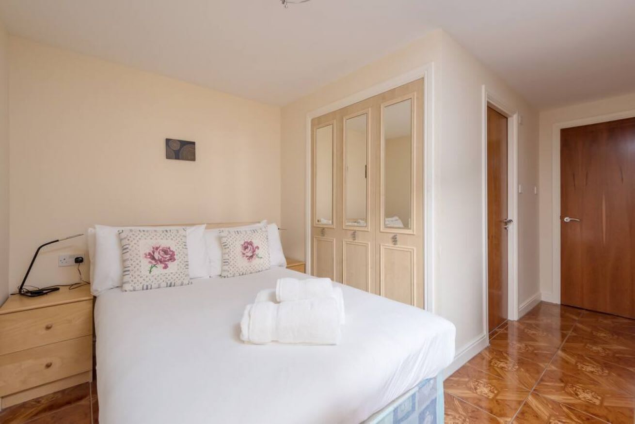 Een slaapkamer met een bed, nachtkastje, kledingkast en een deur.